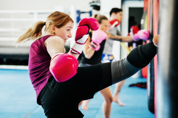 A female adult practicing kickboxing, wearing red gloves, with one leg extended towards punching bag